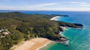 Vista aérea de una zona costera con playa, colinas boscosas y una vista despejada del océano.