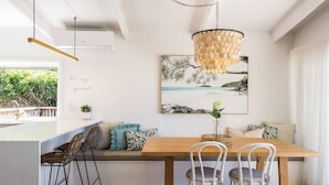 Una cocina moderna con una isla de madera, taburetes, una mesa de comedor con sillas y una lámpara de araña decorativa de gran tamaño.