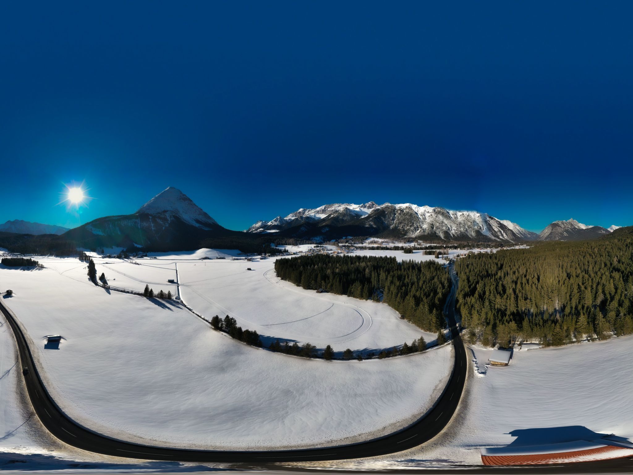 Un paysage enneigé avec une route sinueuse, une chaîne de montagnes et un ciel dégagé.