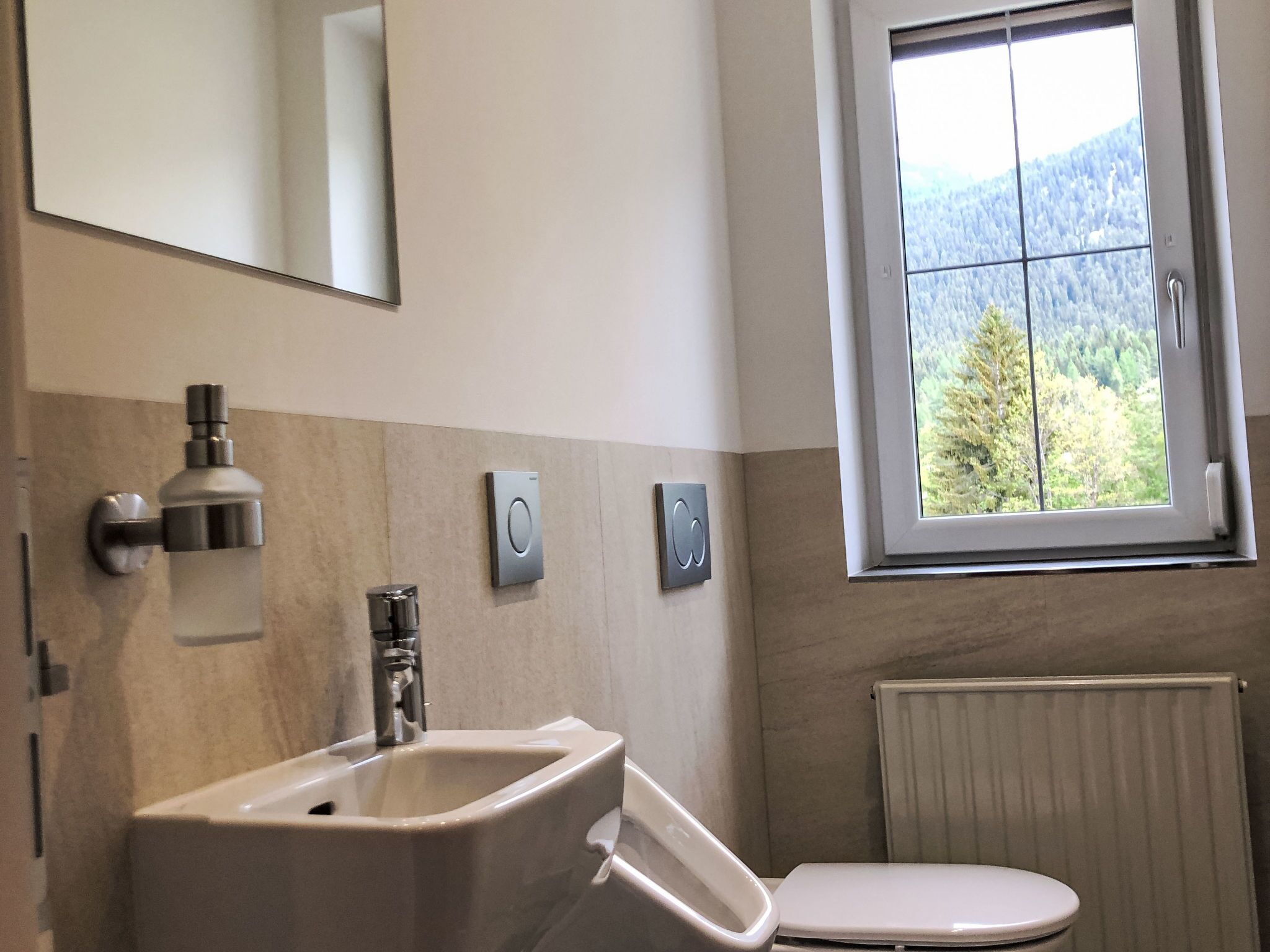 A bathroom with a sink, toilet, and a window with a view of a forest.