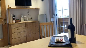 Een kamer met een houten tafel, een stoel, een aan de muur bevestigde televisie, een klok en een raam met gordijnen.