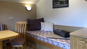 Een kleine kamer met een bed, een houten tafel en een stoel. Er is een wandlamp en een lijst met een bergfoto.