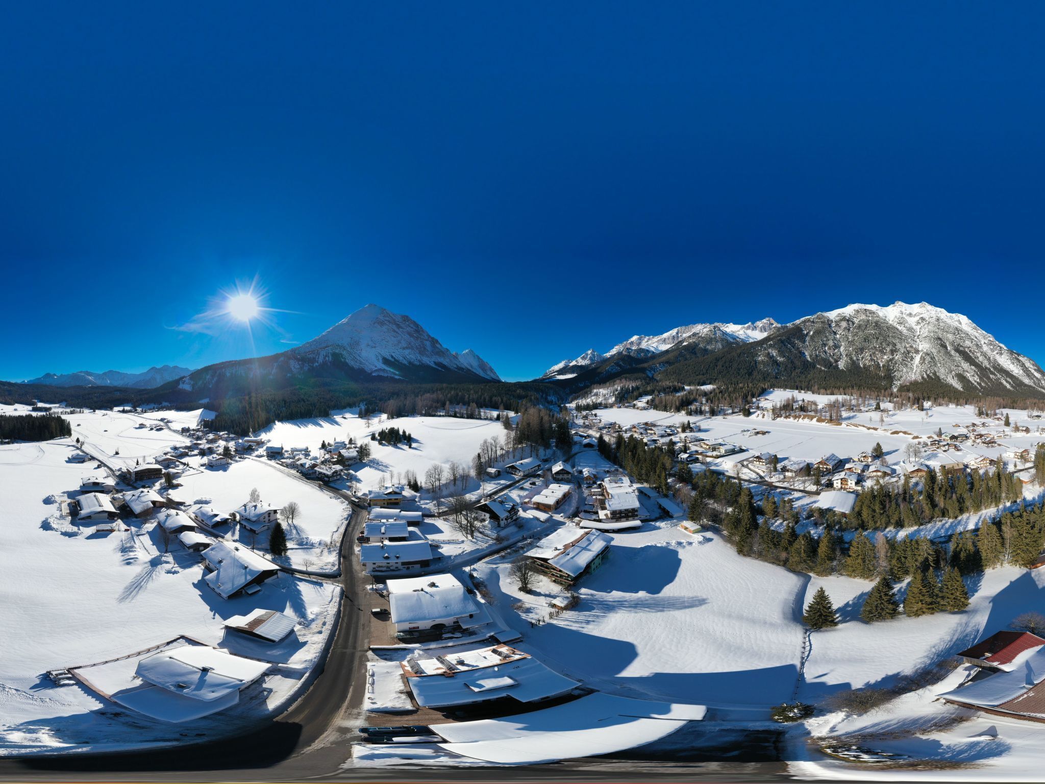 A panoramic view of a snow-covered village with houses, a clear sky, and mountains in the background.