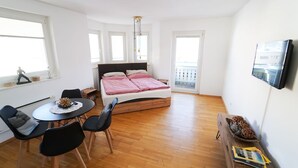 Ein Schlafzimmer mit einem Bett, einem Schreibtisch, zwei Stühlen, einem Fernseher und einem Balkon.