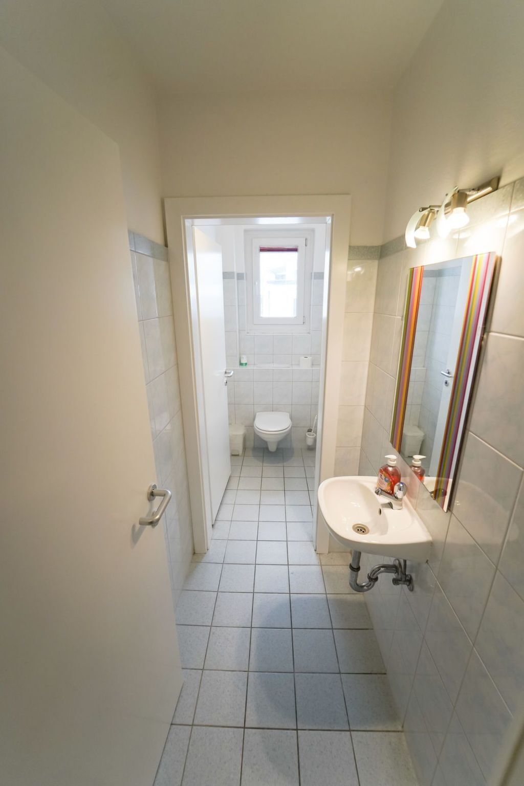A narrow bathroom with a white sink, a mirror, and a toilet.