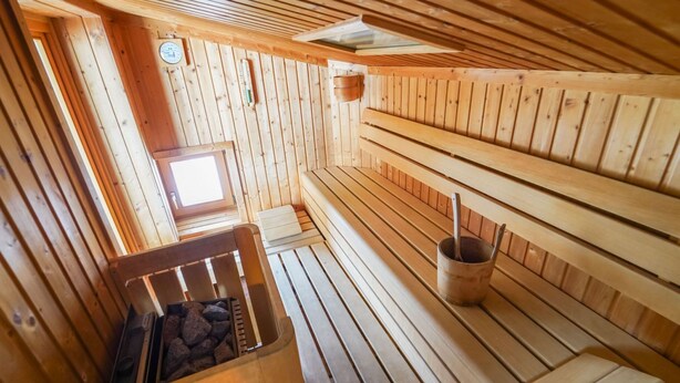 Ein Saunaraum mit Holzbänken, einer stein gefüllten Liege und einem kleinen Fenster.