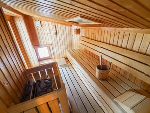 A sauna room with wooden benches, a stone-filled basin, and a small window. - Schlafgut Küssler in Zell am See by Interhome (Zell am See)