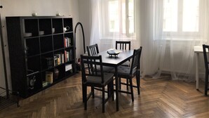 Un comedor con una mesa y sillas, una estantería y ventanas amplias con cortinas ligeras.