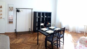 Un comedor con suelo de madera en patrón de espiga, una mesa de comedor negra con platos y vasos blancos, y una estantería negra con repisas.