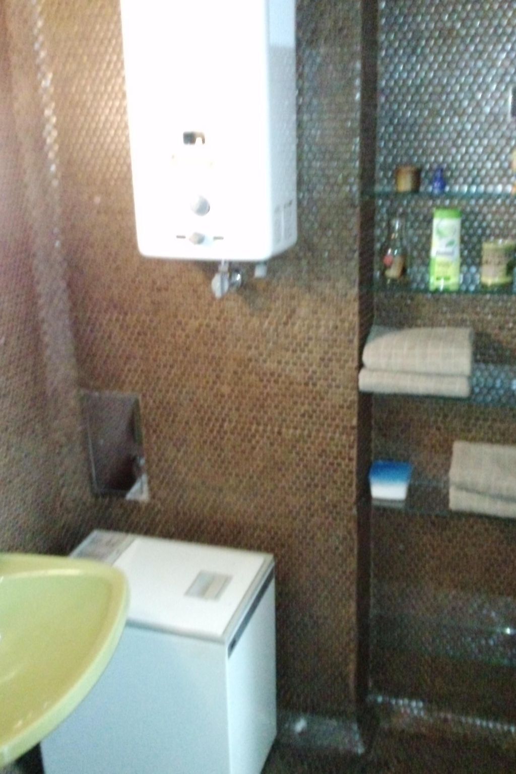 A small room with a white washing machine, a yellow sink, and a metal shelf with toiletries.