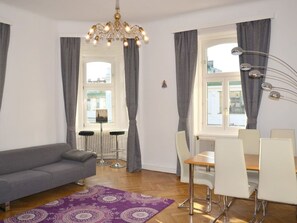 A modern living room with a grey sofa, a dining table with chairs, a chandelier, and a view of the city through large windows with grey curtains. - Vienna1090 by Interhome (Vienna)