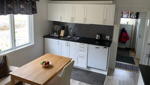 Een kleine keuken met witte kastjes, een zwart aanrecht en een raam met gordijn.