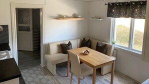 Een compacte woonruimte met een kitchenette, een eethoek met een tafel en stoelen, een bank en een raam met gordijnen.