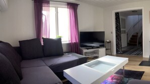 Een moderne woonkamer met een grijze bank, een flatscreen televisie en een salontafel met glazen blad.