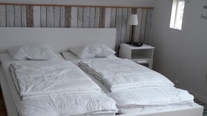 A neatly made double bed with white bedding, a bedside table with a lamp, and a small window with a view of the outdoors.
