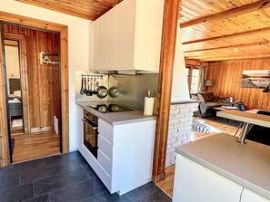 A compact kitchen with white cabinets, a stove, and hanging utensils. - mit Garten, Grill und Terrasse by Interhome (Hultsfred)