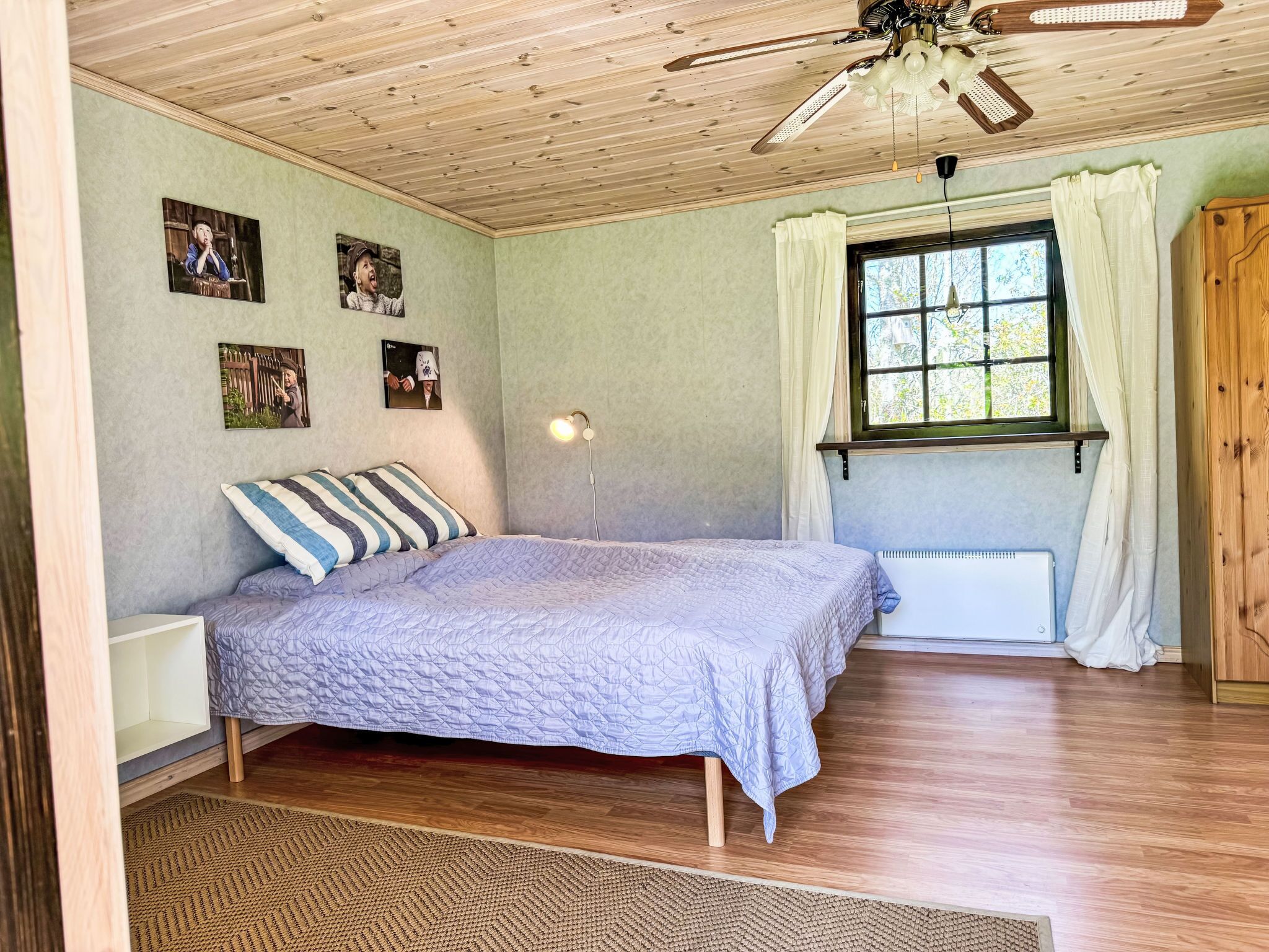 A bedroom with a bed, a ceiling fan, a window with curtains, and wall-mounted pictures.