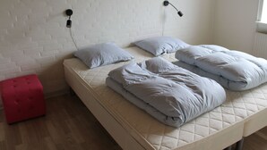 En säng med en stoppad madrass, två kuddar, en röd pall och en vit tegelvägg med två vägglampor.