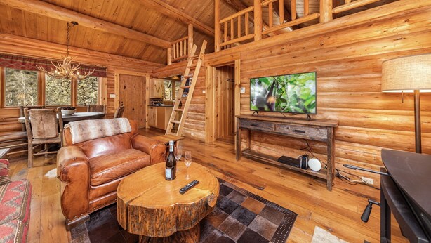 A wooden cabin interior with a leather sofa, a wooden coffee table, a television, and a fireplace. - Jackson Hole Cabin on 4+ wooded acres in Wilson, WY (Wilson)