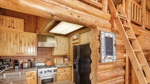 A log cabin interior with a kitchen featuring wooden cabinets, granite countertops, a stove, and a refrigerator. - Jackson Hole Cabin on 4+ wooded acres in Wilson, WY (Wilson)
