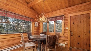 A wooden cabin interior with a round dining table, chairs, a chandelier, and a large wooden door. - Jackson Hole Cabin on 4+ wooded acres in Wilson, WY (Wilson)