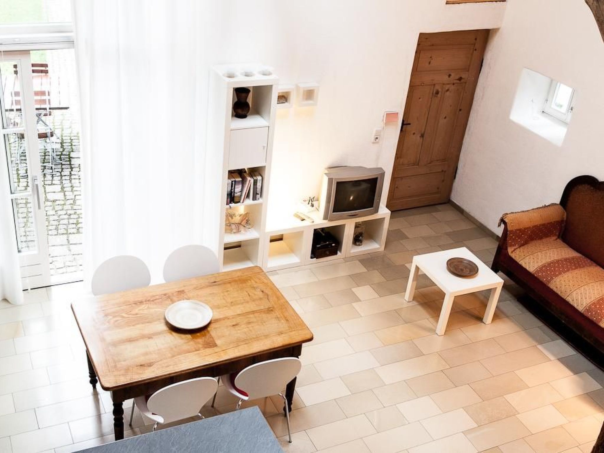 A cozy living room with a wooden table, white chairs, a sofa, and a TV on a stand.