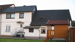 A two-story house with a dark tiled roof, a small wooden playhouse, and a well-maintained lawn. - Appartement in Steinhude mit Terrasse und Garten by Interhome (Wunstorf)