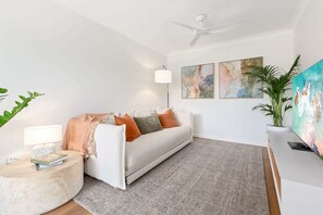 Ein modernes Wohnzimmer mit einem weißen Sofa, einem runden Beistelltisch, einer Stehlampe und abstrakten Bildern an der Wand.