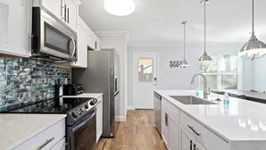 A modern kitchen with white cabinetry, a black stove, a microwave, and a refrigerator. - Nice 4-bedroom house with walking distance to theAT&T stadium (Arlington)