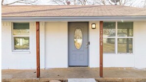 A single-story house with a gray door, a small porch, and a satellite dish on the roof. - Nice 4-bedroom house with walking distance to theAT&T stadium (Arlington)