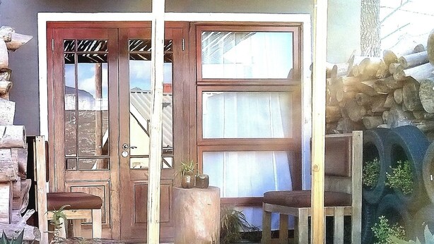 Uma casa de madeira rústica com uma grande porta da frente, um pequeno alpendre e uma parede de pedra.