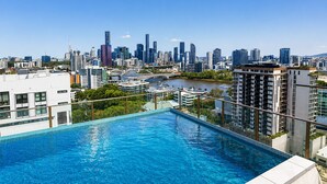 Schwimmbad auf dem Dach mit Blick auf eine Stadtlandschaft, moderne Gebäude und einen Fluss.