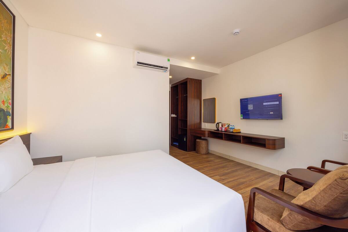 A hotel room with a large bed, a TV mounted on the wall, a wooden floor, and a small seating area with a chair.