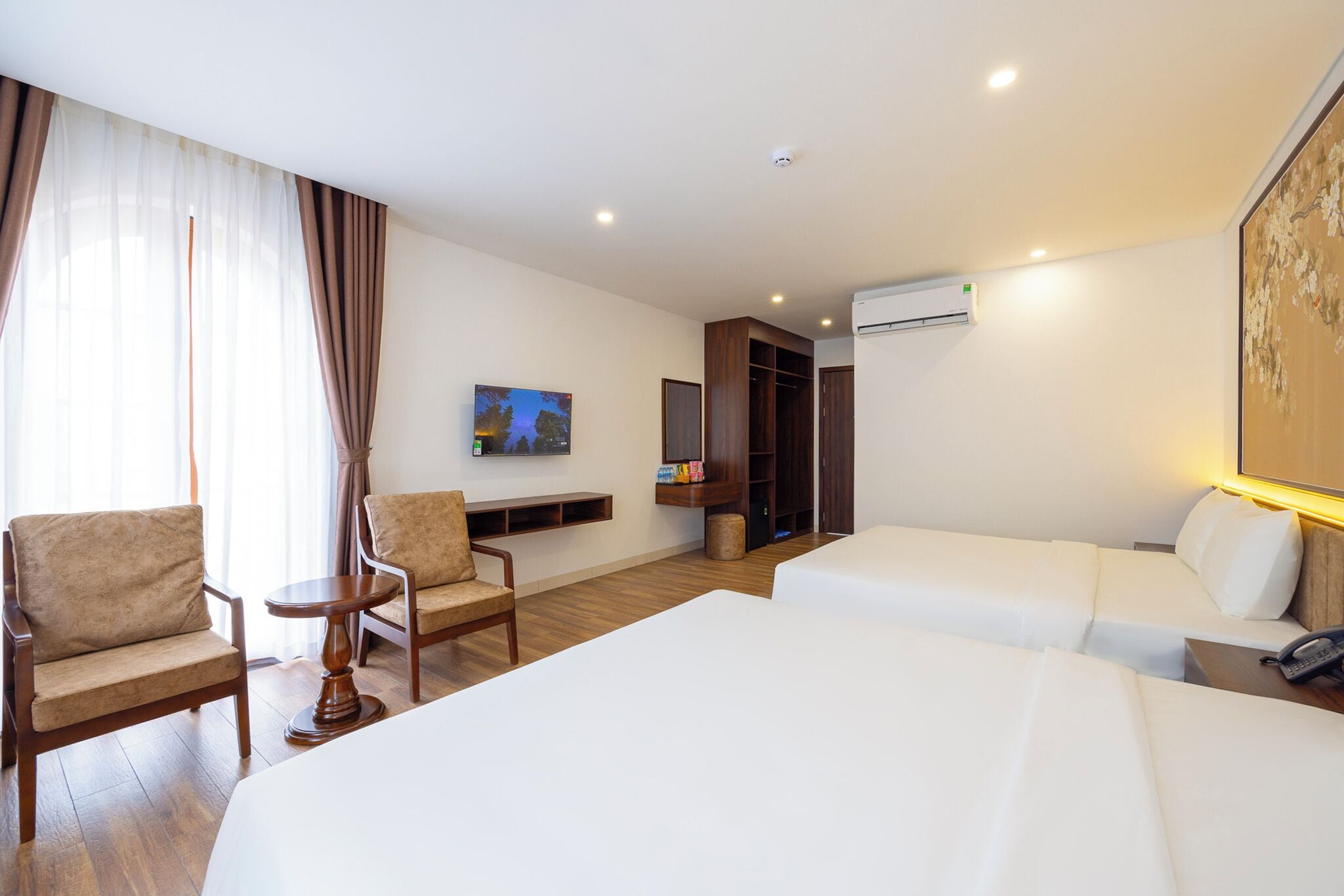 A hotel room with two beds, a desk, a chair, a TV, and a wardrobe.