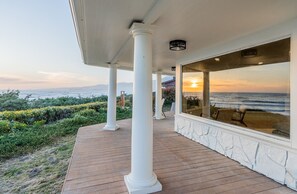 Un espace extérieur abrité, avec vue sur l’océan, des colonnes blanches et une terrasse en bois.