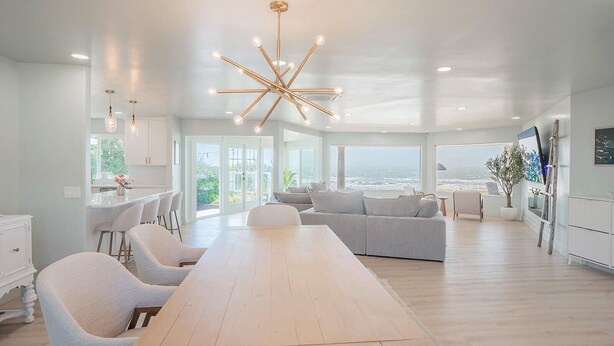 A spacious living area with a large wooden table, a grey sofa, and a modern chandelier. - Pacific Edge  Private Beach Access, Oceanfront Luxury Retreat 4BR 3BA (Smith River)