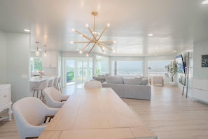 Ein geräumiger Wohnbereich mit einem großen Holztisch, einem grauen Sofa und einer modernen Kronleuchter.