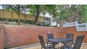 Un patio al aire libre con pared de ladrillo, una mesa con cuatro sillas y una valla de madera al fondo.