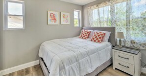 Un dormitorio con cama, mesita de noche y ventana con cortinas.