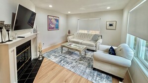 Un salon moderne avec une cheminée, un grand téléviseur à écran plat, un canapé, une table basse et une grande fenêtre.