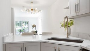 Une cuisine moderne avec des meubles blancs, un évier en acier inoxydable et un luminaire.
