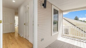 Une véranda couverte avec une terrasse en bois, une porte blanche et une fenêtre donnant sur le ciel.