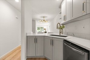 Una cocina moderna con gabinetes grises, lavavajillas de acero inoxidable y encimera blanca.