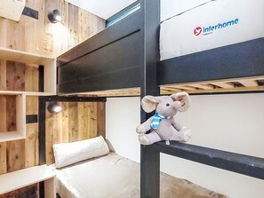 Ein Etagenbett mit einer Kuscheltierfigur auf dem oberen Bett, einem weißen Kopfkissen und einer Wand mit einem Logo.
