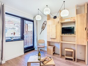 Un ambiente moderno con un'ampia finestra, una zona pranzo con una bottiglia e dei bicchieri, e una TV su un mobile in legno.