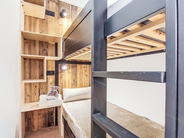 A compact room with a bunk bed, wooden shelving, and a small table with a plush toy. - Les Olympiades by Interhome (Val Thorens)