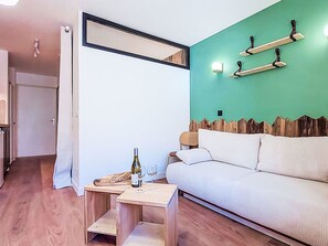 A modern living room with a sofa, a small wooden table with a bottle and glasses, a green accent wall, and a door leading to another room. - Les Olympiades by Interhome (Val Thorens)