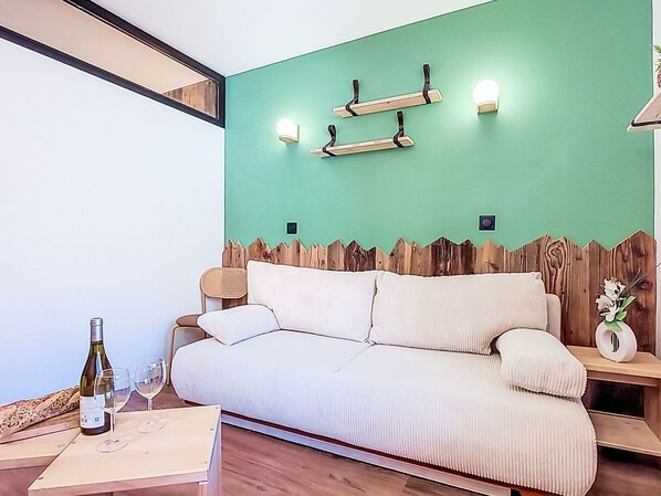 Un soggiorno moderno con una parete verde a contrasto, un divano bianco, una testiera di legno e un tavolino con una bottiglia e un bicchiere.