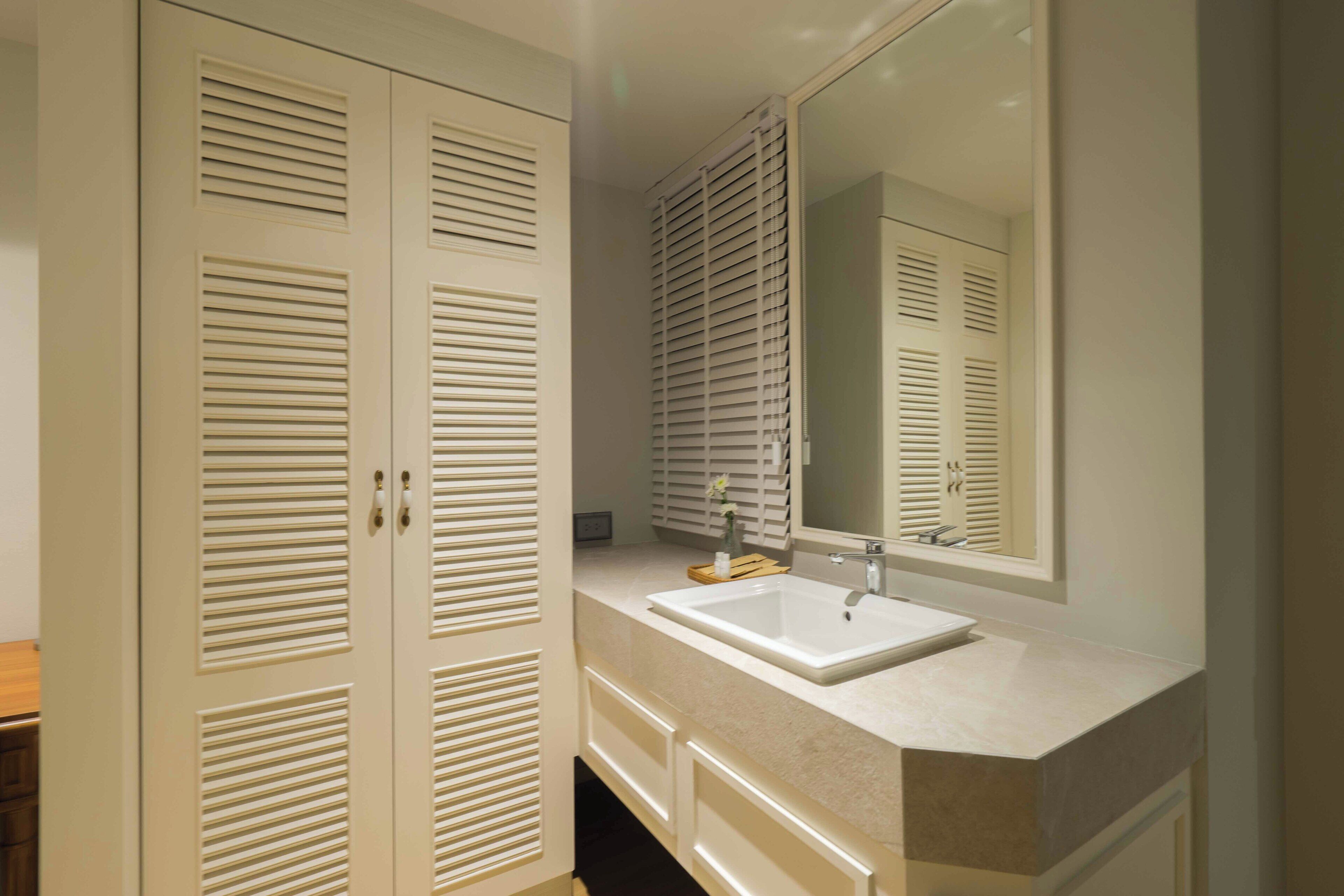 A bathroom with a white vanity, a large mirror, and a double door with louvered panels.