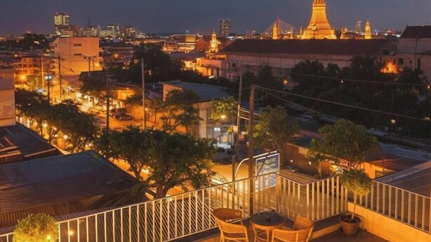 A rooftop terrace with outdoor furniture, a view of a cityscape at dusk, and a prominent building in the distance. - TUAN Hotel Bangkok near Wat Arun (Bangkok)